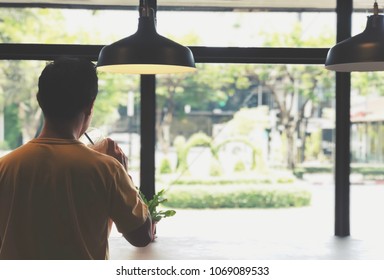 Rear view of young man looking outside coffee shop. Young man drinking ice coffee and standing alone in coffee shop. Man, Hanging lamp and ice coffee. Chill, relax, alone concept. Copy space