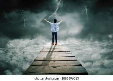 Rear View Of Young Man Looks Bravery While Standing On The Wooden Bridge And Looking At Lightning At Cloudy Sky