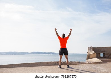 Rear View Of Young Man Raising Arms On Beach