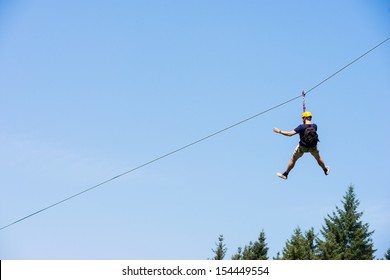 Rear view of young man riding on zip line against blue sky