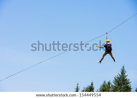 Rear view of young man riding on zip line against blue sky
