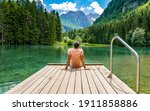 Rear view of young  man sitting on wooden deck by beautiful lake in mountains  Green, spring, outdoors  Zgornje Jezersko, Slovenia