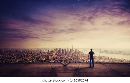 Rear view of young man standing on the rooftop of a skyscraper watching sunset over the big city horizon. Businessman on the roof getting inspired and motivated. - Powered by Shutterstock