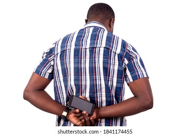 Rear View Of Young Man Standing Against White Background And Holding Mobile Phone Behind His Back.