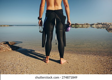 Rear View Of Young Man Standing On Lake Wearing Wetsuit. Cropped Shot Of A Triathlete Preparing For A Race Wearing A Wetsuit Prior To The Swim Start.