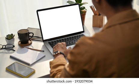 Rear View Of Young Man Using Laptop Computer Checking Email In Morning At Home.