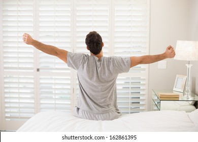 Rear view of a young man waking up in bed and stretching his arms - Powered by Shutterstock