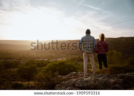 Rear view of young man and woman standing at mountain cliff looking at sunrise
