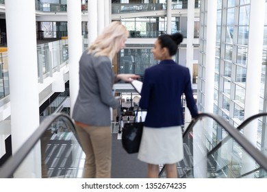 Rear view of young multi-ethnic businesswomen interacting with each other while using escalator in modern office - Powered by Shutterstock