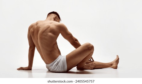 Rear view of young muscular man with relief body, strong back sitting shirtless in boxers isolated over white studio background. Concept of male beauty, body care, fitness, sport, health - Powered by Shutterstock