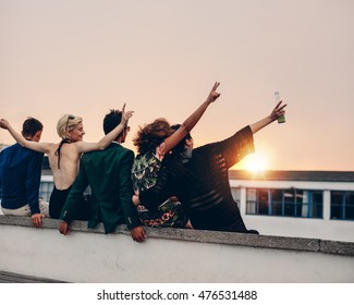 Rear view of young people partying on terrace with drinks at sunset. Young men and women enjoying drinks on rooftop in evening. - Shutterstock ID 476531488