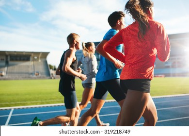 Rear view of young people running together on race track. Young athletes practicing a run on athletics stadium track.