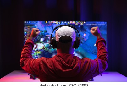 Rear View Young Player Video Computer Pc. Young Man Sitting On Chair In Game Station.Streamer Man Wearing Headphone  Playing Action Game Online In The Darkroom.