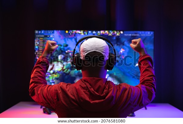 Rear view young Player video\
computer pc. Young man sitting on chair in game station.Streamer\
man wearing headphone  playing action game online in the\
darkroom.