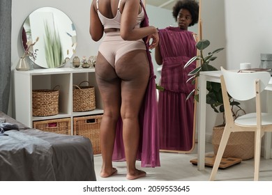 Rear View Of Young Plus Size Woman Trying On New Dress In Front Of Mirror In Bedroom