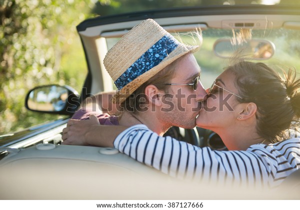 Rear view. A young romantic\
couple kissing in a convertible car on a country road. Shot with\
flare