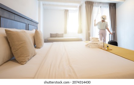 Rear view of young tourist woman looking to view outside window in hotel bedroom after check-in. Conceptual of travel and vacation lifestyle.
