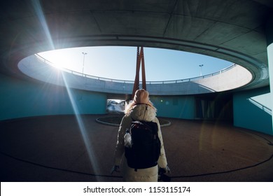 Rear view of young traveler woman in white winter coat with backpack standing under the bridge in Norway. Urban background. Circle. Modern architecture concept. - Powered by Shutterstock