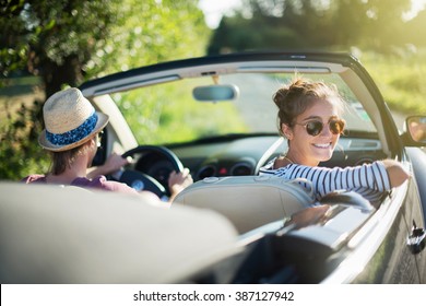 Rear view. Young trendy couple happy to drive his convertible car on a country road in summer. Shot with flare