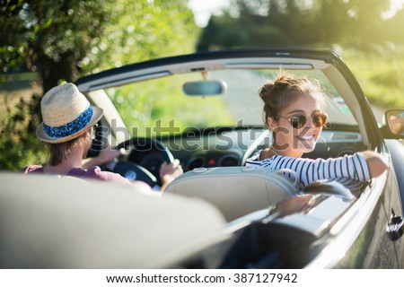 Rear view. Young trendy couple happy to drive his convertible car on a country road in summer. Shot with flare