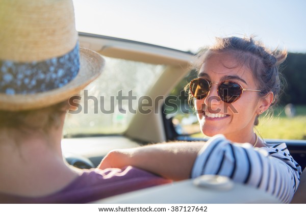 Rear view. Young\
trendy couple happy to drive his convertible car on a country road\
in summer. Shot with flare