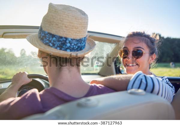 Rear view. Young trendy couple happy to drive\
his convertible car on a country road in summer. There are some\
cows at the background. Shot with\
flare