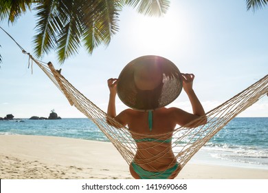 Rear View Of Young Woman In Bikini And Hat Sitting On Hammock On The Beach - Shutterstock ID 1419690668