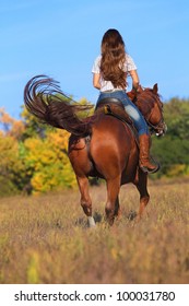 Rear view of young woman in blue jeans riding a horse