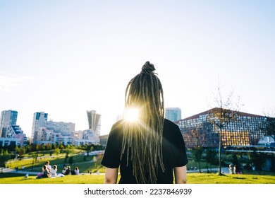 Rear view young woman with dreadlocks in park. Modern park on background.
