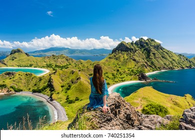 Rear view of a young woman enjoying the awesome view of Padar Island, while sitting on the top of a volcanic mountain during summer vacation in Indonesia - Powered by Shutterstock