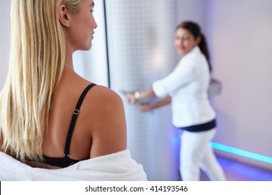 Rear view of young woman going for cryotherapy with nurse standing at the door of cyrosauna in background.