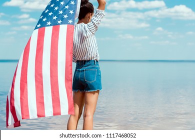 rear view of young woman holding american flag in front of sea, independence day concept - Powered by Shutterstock