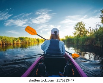 Rear view of a young woman in a kayak rafting down a river at dawn. Location Seret, Ukraine. Active recreation in the open air. Female enjoying water sport on vacation. Discover the beauty of earth.