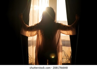 Rear view young woman opens curtains of bedroom window. Young girl is ready for new plans and new challenges. Concept of opening yourself to world, new affairs and new promises - Powered by Shutterstock