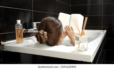 Rear view of young woman relaxing in bath and reading a book. Self-care, education, hygiene and spa - Powered by Shutterstock