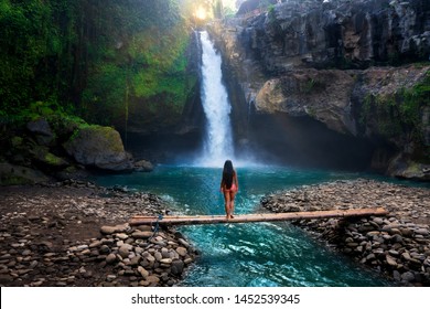 Rear view of young woman standing in front of waterfall with her hands raised. Female tourist with her arms outstretched looking at waterfall. - Powered by Shutterstock