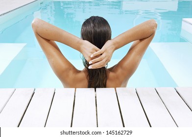 Rear View Of Young Woman In Swimming Pool At Poolside Pulling Back Hair