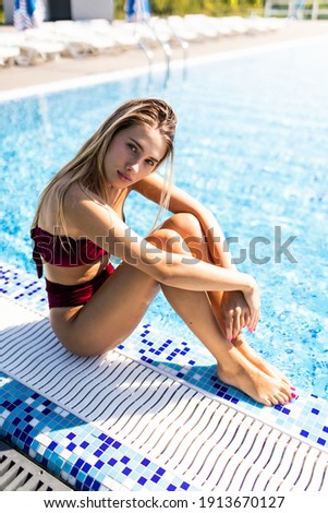 Rear view of young woman in swimming pool resting on poolside