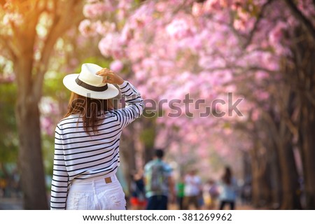Rear view of young woman trying to selfie herself in a park with pink trumpet trees flower.