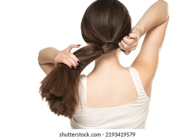 Rear view of a young woman tying her long hair on a white background.