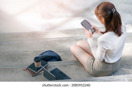 Rear view of young woman using smartphone while sitting on stairs outside.