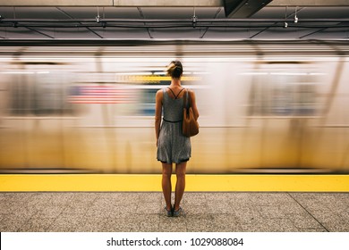 Rear view at young woman waiting for subway train in New York City, USA