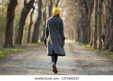 Rear View Of A Young Woman Walking On An Avenue . Travel And Fashion Concept.