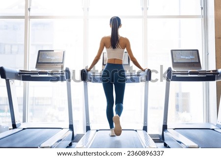 Rear view of young woman walking on treadmill