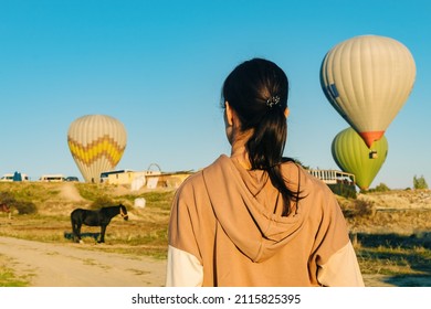 Rear View Young Woman Watching Hot Air Balloons Taking Off In Cappadocia, Goreme, Turkey