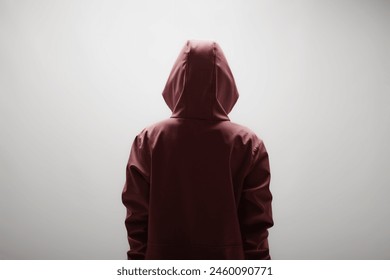 Rear view of a young woman wearing a maroon hoodie, standing against a plain light background. The image evokes a sense of mystery and anonymity. - Powered by Shutterstock