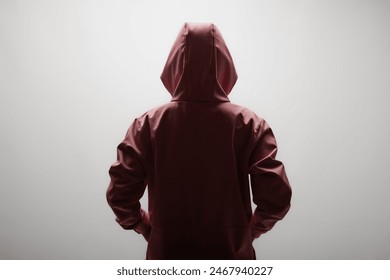 Rear view of a young woman wearing a maroon hoodie, standing against a plain light background. The image evokes a sense of mystery and anonymity. - Powered by Shutterstock