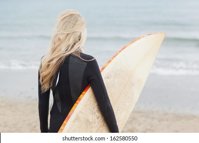 Rear View Of A Young Woman In Wet Suit Holding Surfboard At Beach