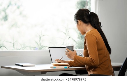 Rear view of young woman writing note and searching information on internet on laptop at home. Work from home - Powered by Shutterstock