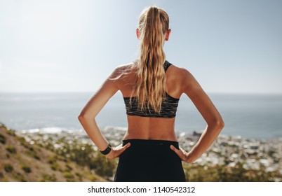 Rear view of young woman's standing with her hands on hips and looking at a view. Female runner taking break from running. - Powered by Shutterstock